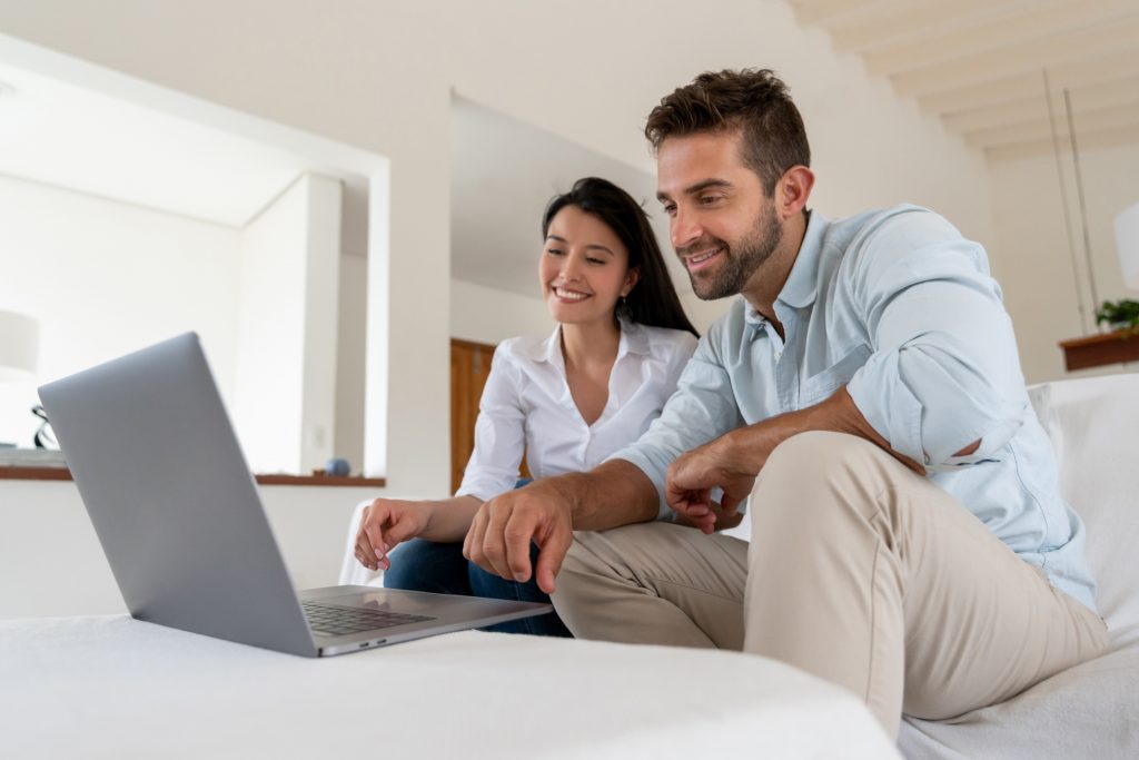 Happy couple at home looking at social media on a laptop computer and smiling â lifestyle concepts